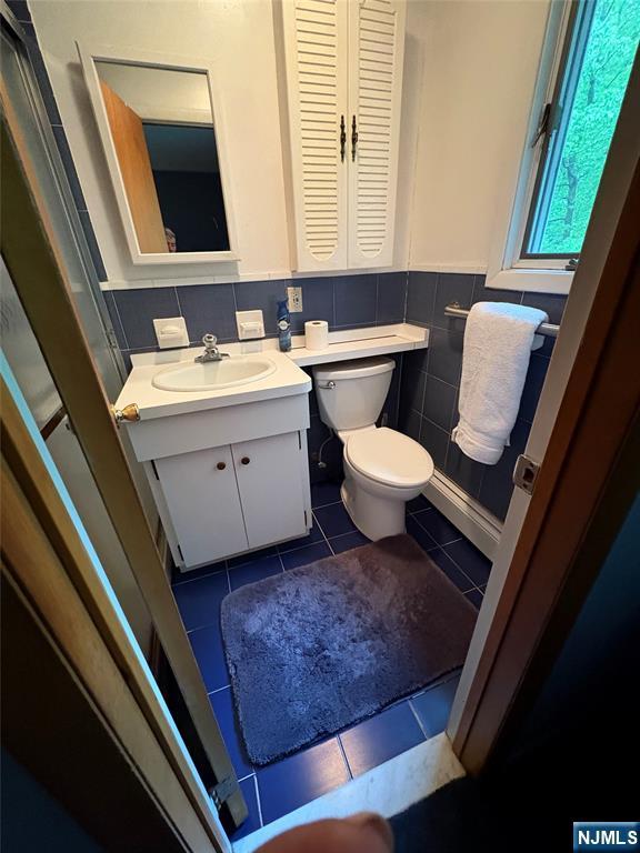 103 Northwood Ave, Demarest, NJ 07627 - bathroom featuring tile patterned flooring, toilet, vanity, tile walls, and a wainscoted wall