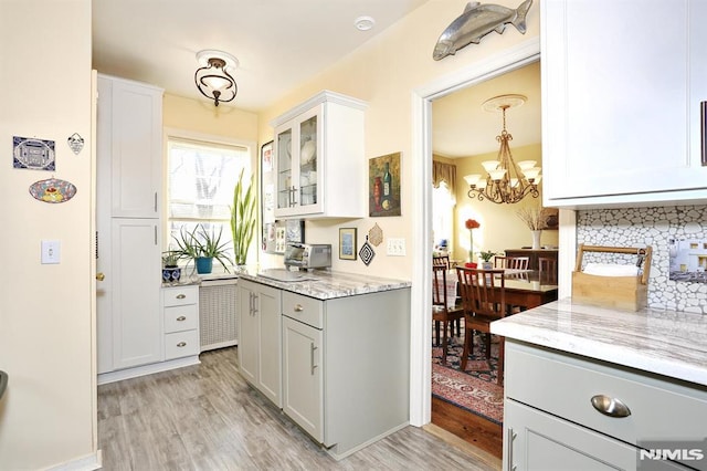 kitchen with light stone countertops, pendant lighting, white cabinets, and light wood-type flooring