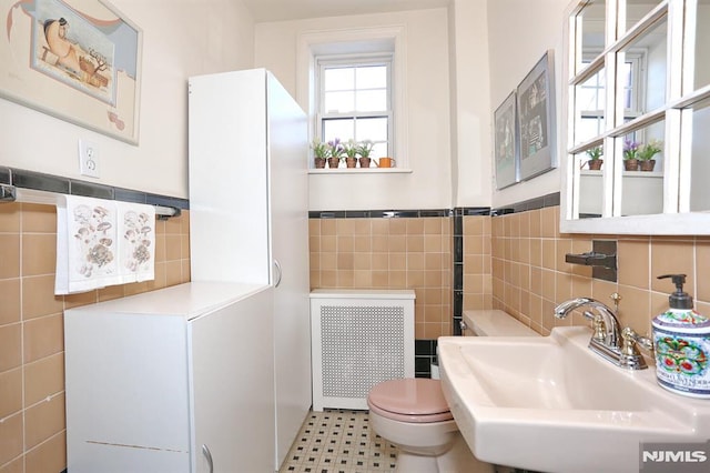 bathroom with toilet, radiator, sink, and tile walls