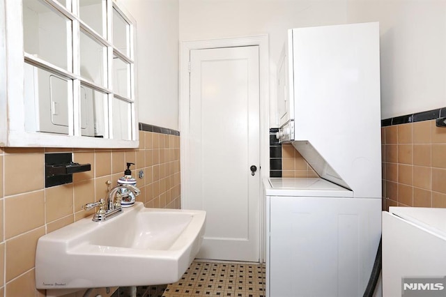 bathroom with tile walls, sink, and stacked washer / dryer