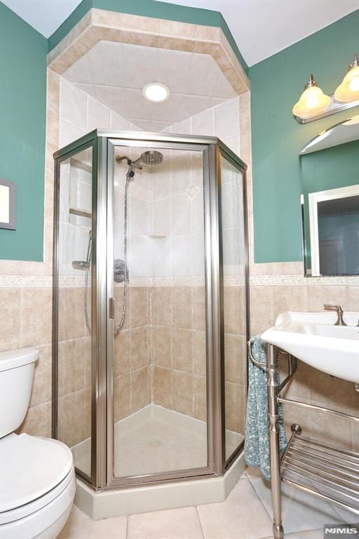 bathroom with tile walls, tile patterned floors, a shower with door, and toilet