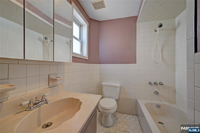 full bathroom with tile patterned floors, toilet, tiled shower / bath, tile walls, and vanity