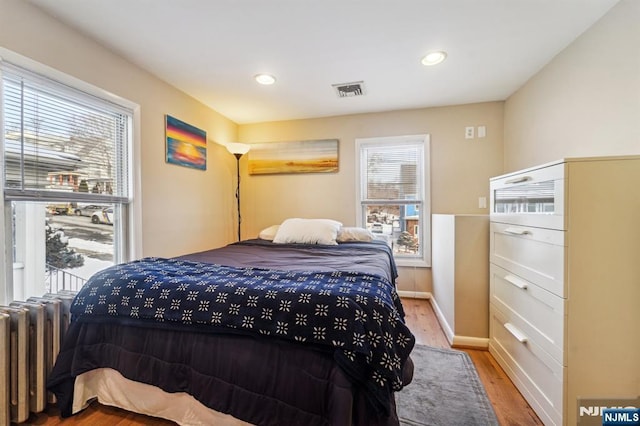 bedroom with multiple windows, radiator heating unit, and light hardwood / wood-style flooring