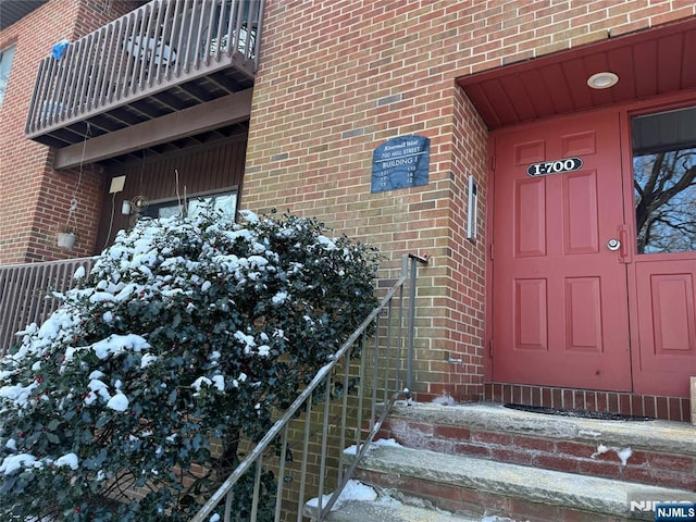 snow covered property entrance with a balcony