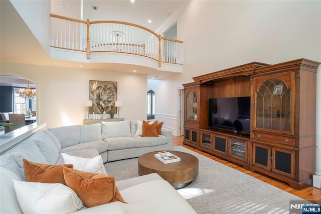 living area with arched walkways, a notable chandelier, a high ceiling, wood finished floors, and visible vents