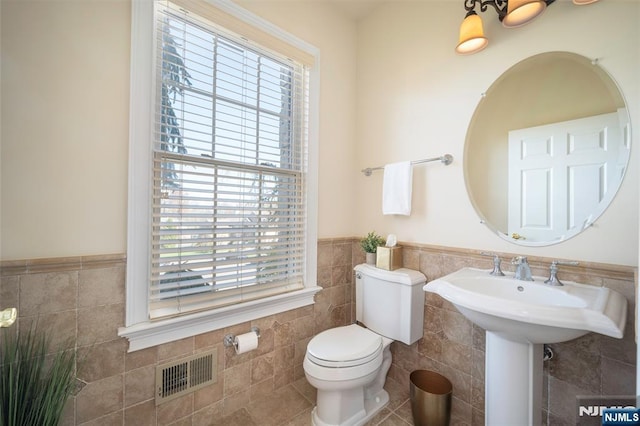 bathroom with tile patterned flooring, toilet, a wainscoted wall, visible vents, and tile walls