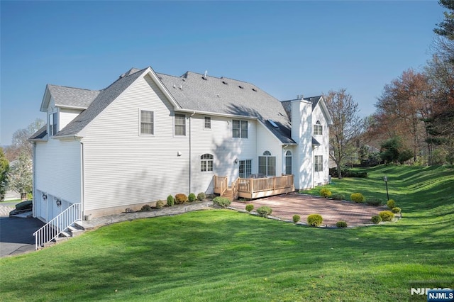 rear view of property featuring a shingled roof, a lawn, a patio area, a deck, and driveway