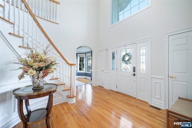 foyer entrance with visible vents, arched walkways, a high ceiling, stairs, and light wood-style floors