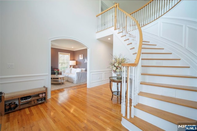 stairway featuring arched walkways, crown molding, wood finished floors, and a decorative wall