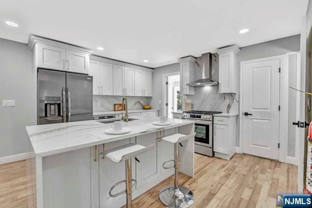 kitchen with a kitchen bar, sink, light stone counters, stainless steel appliances, and wall chimney range hood