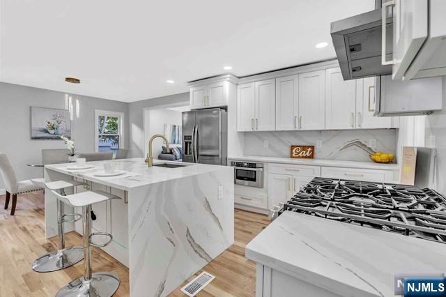 kitchen featuring sink, a center island with sink, stainless steel appliances, light stone counters, and a kitchen bar