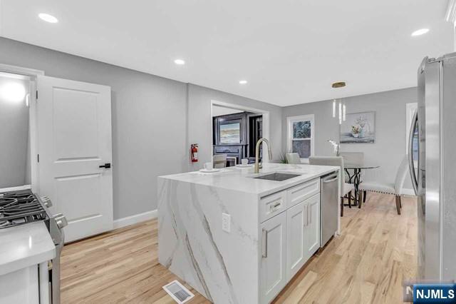 kitchen featuring white cabinetry, an island with sink, sink, light hardwood / wood-style floors, and stainless steel appliances