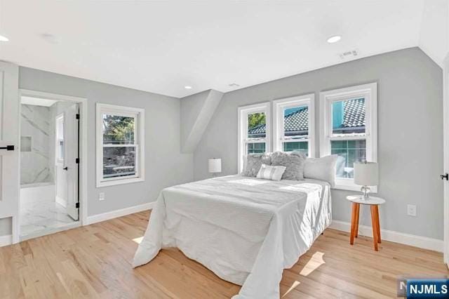 bedroom with ensuite bathroom, multiple windows, and light hardwood / wood-style flooring