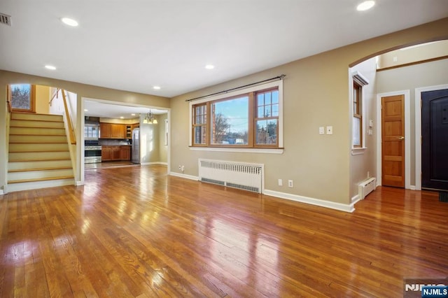 unfurnished living room with hardwood / wood-style floors, a baseboard radiator, radiator heating unit, and an inviting chandelier