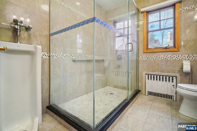 bathroom with radiator, water heater, tile walls, a shower with door, and tile patterned floors