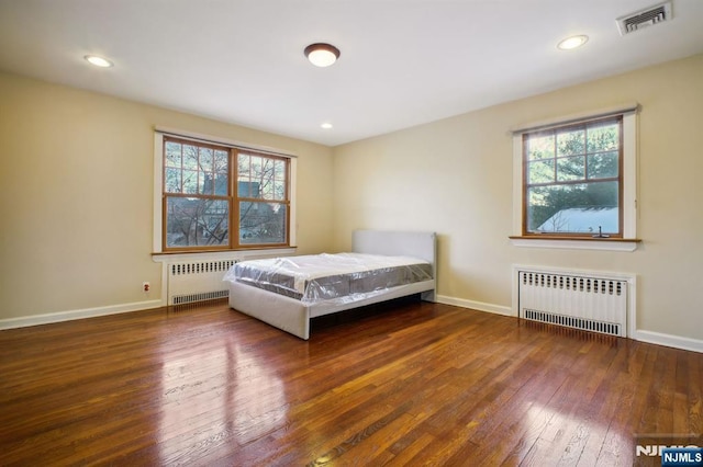 unfurnished bedroom with dark wood-type flooring, radiator heating unit, and multiple windows