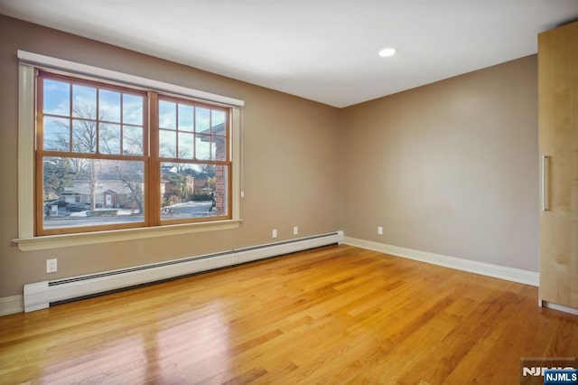 unfurnished room with baseboard heating and light hardwood / wood-style floors