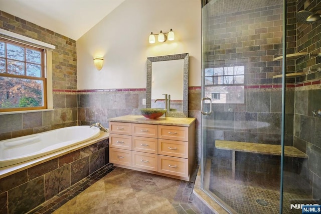 bathroom featuring vanity, independent shower and bath, vaulted ceiling, and tile walls