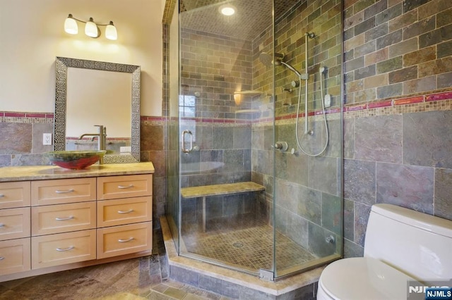 bathroom with vanity, a shower with shower door, tile walls, and toilet