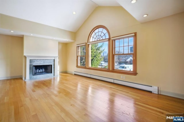 unfurnished living room with a baseboard radiator, lofted ceiling, a high end fireplace, and light hardwood / wood-style floors