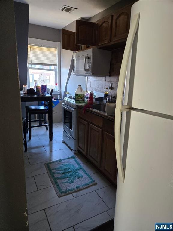 kitchen featuring light tile patterned flooring, sink, decorative backsplash, dark brown cabinets, and white appliances