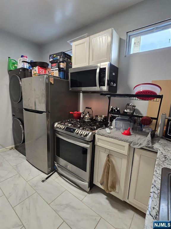 kitchen with light stone counters, appliances with stainless steel finishes, and stacked washer / drying machine