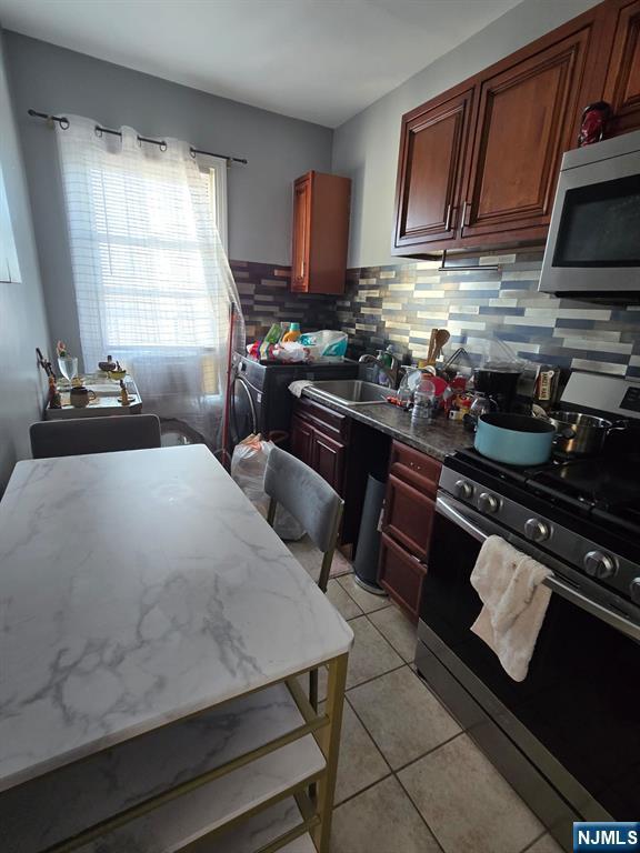 kitchen featuring light tile patterned flooring, sink, light stone counters, stainless steel appliances, and decorative backsplash