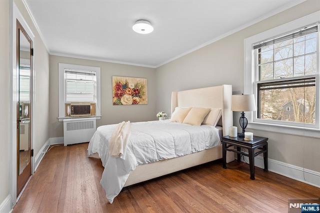 bedroom with hardwood / wood-style flooring, ornamental molding, radiator heating unit, and multiple windows