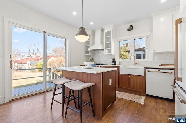 kitchen featuring a kitchen island, pendant lighting, sink, white dishwasher, and wall chimney exhaust hood