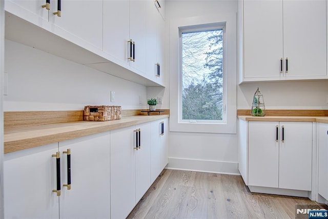 bar with a healthy amount of sunlight, white cabinets, and light hardwood / wood-style flooring