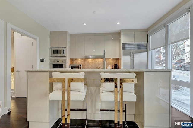 kitchen featuring built in appliances, backsplash, a kitchen island, and a kitchen bar