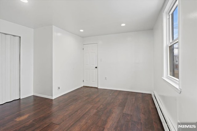 unfurnished room featuring baseboard heating and dark hardwood / wood-style flooring