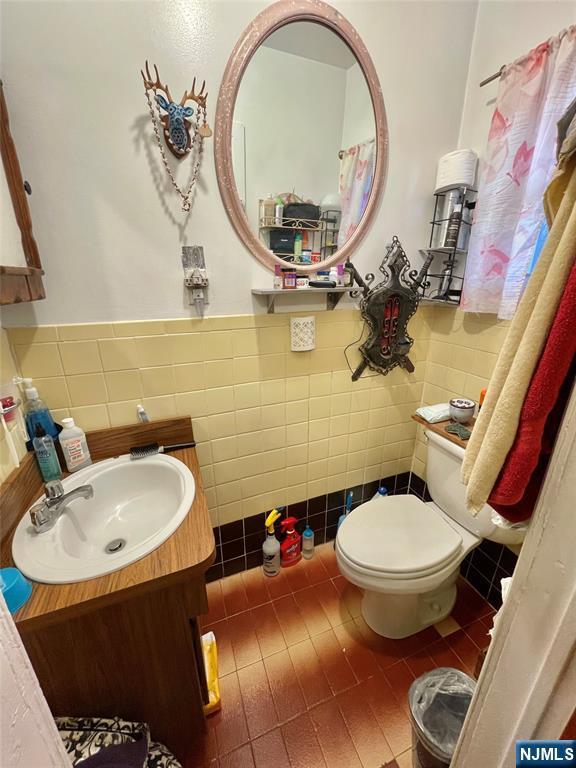 bathroom featuring vanity, toilet, tile patterned flooring, and tile walls