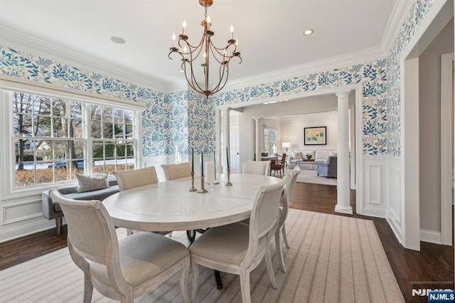 dining space featuring dark hardwood / wood-style flooring, a notable chandelier, crown molding, and decorative columns