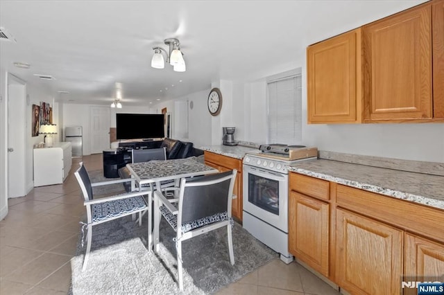 kitchen featuring light tile patterned flooring, white gas range, light stone counters, and refrigerator