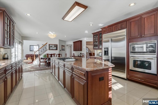 kitchen with decorative backsplash, a center island, built in appliances, light tile patterned floors, and light stone countertops