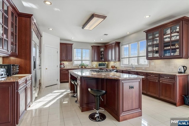 kitchen featuring sink, light stone counters, a center island, appliances with stainless steel finishes, and decorative backsplash