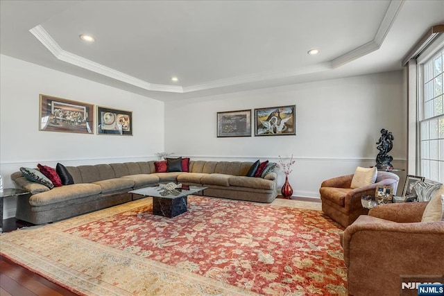 living room with crown molding, wood-type flooring, and a tray ceiling