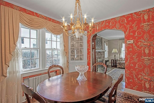 dining area with radiator, hardwood / wood-style floors, a fireplace, ornamental molding, and a chandelier