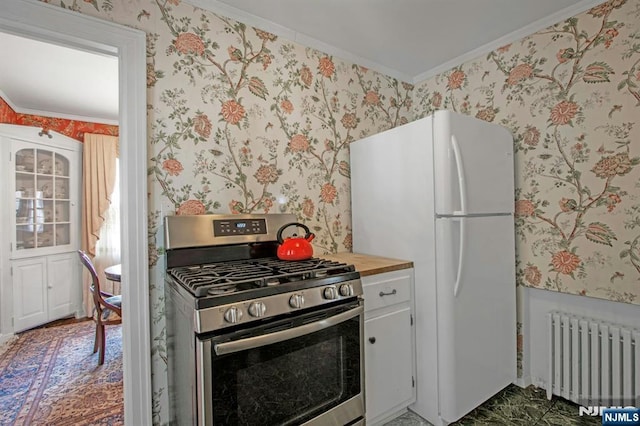 kitchen with white cabinetry, white refrigerator, ornamental molding, stainless steel range with gas cooktop, and radiator heating unit