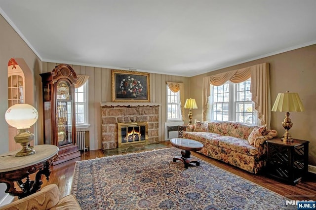 living room featuring hardwood / wood-style flooring, ornamental molding, and a stone fireplace