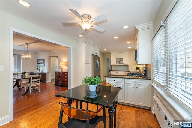 dining space featuring ceiling fan with notable chandelier, radiator heating unit, and light hardwood / wood-style floors