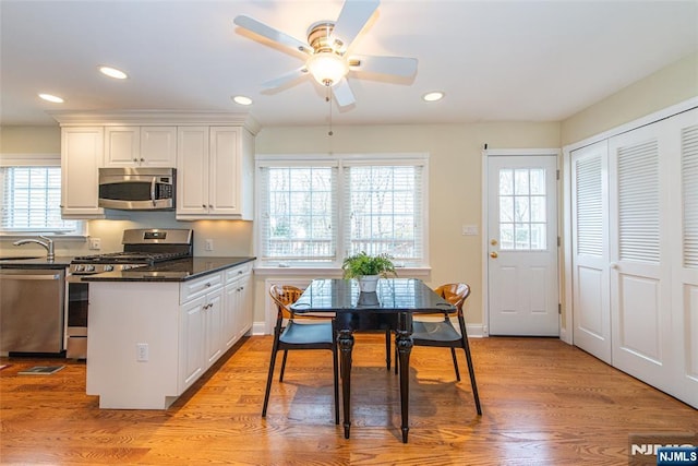 kitchen with stainless steel appliances, white cabinetry, light hardwood / wood-style flooring, and dark stone counters