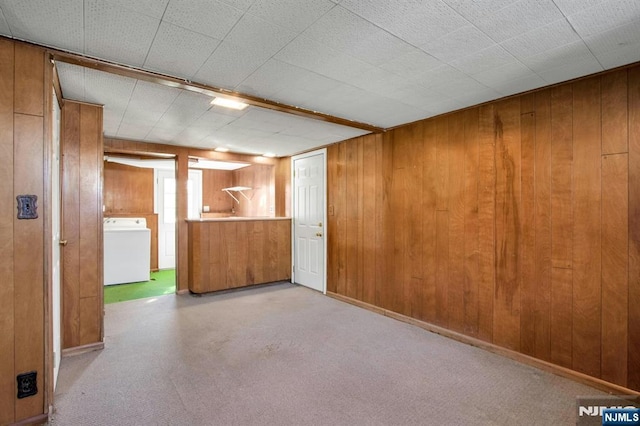 basement with light carpet, washer / clothes dryer, and wood walls