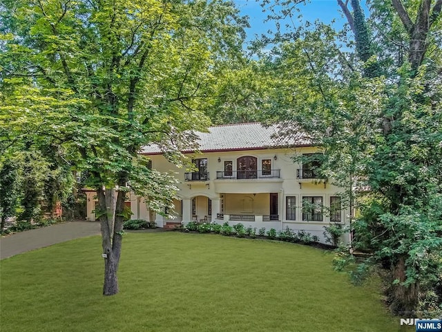 mediterranean / spanish-style house featuring a front yard, a tile roof, a balcony, and stucco siding