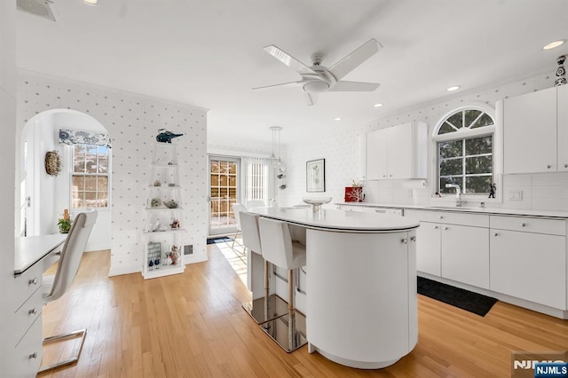 kitchen featuring sink, white cabinetry, a center island, hanging light fixtures, and light hardwood / wood-style floors