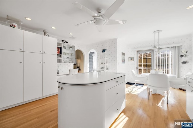 kitchen featuring white cabinetry, hanging light fixtures, a center island, ceiling fan, and light wood-type flooring