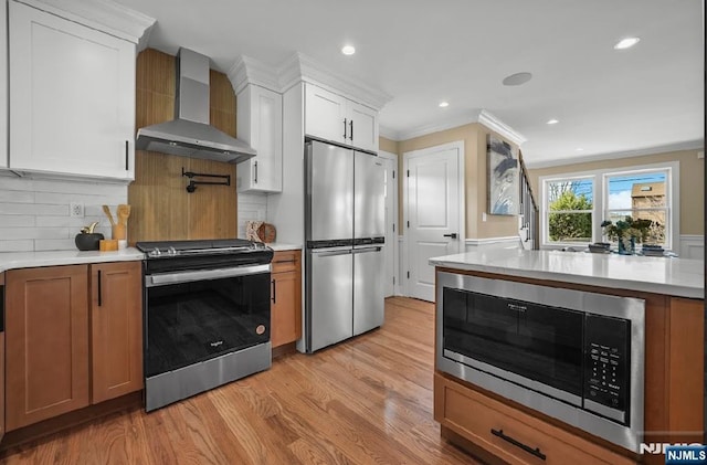 kitchen with white cabinetry, stainless steel appliances, light hardwood / wood-style flooring, and wall chimney range hood