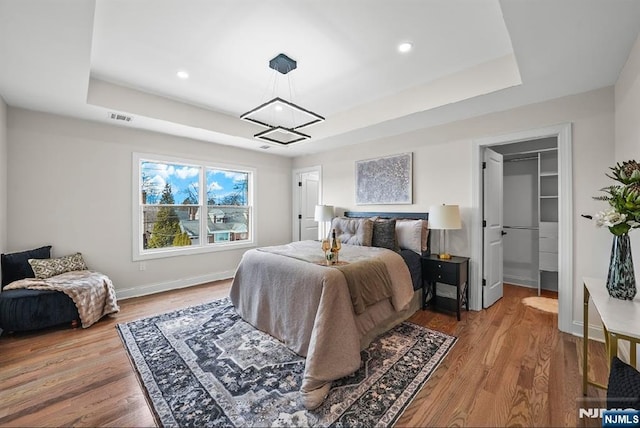 bedroom featuring a tray ceiling, a walk in closet, and light wood-type flooring