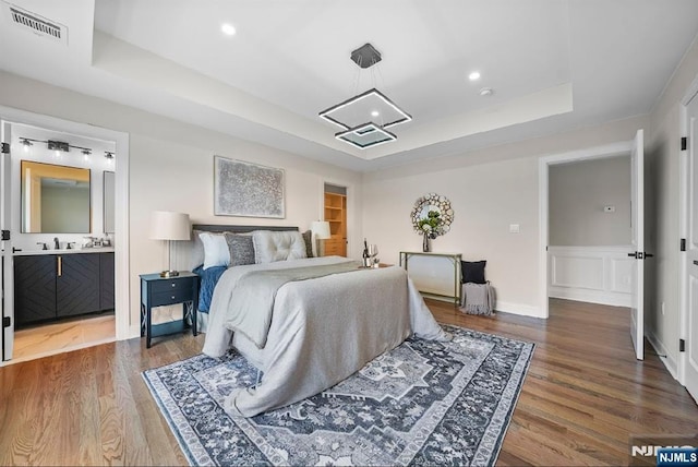 bedroom featuring ensuite bathroom, sink, hardwood / wood-style floors, and a tray ceiling